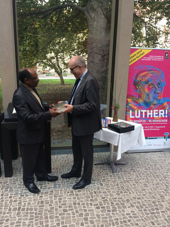 Im Bild gratuliert Stefan Rhein dem 200.000sten Besucher, Kakule Molo, und überreicht ihm als Geschenk einen Ausstellungskatalog.